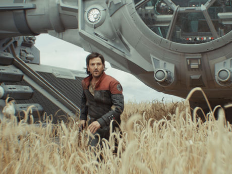 Diego Luna walking on a wheat field, with a spaceship parked behind him.
