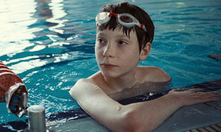 Everett Blunck, rocking swim goggles, hanging out in the water at the edge of a pool.