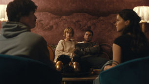 Carey Mulligan and Oscar Isaac sitting next to each other on a couch, looking at Charles Melton and Cailee Spaeny who are sitting across the table.