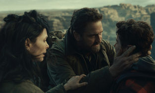 Gerard Butler grabbing Roman Griffin Davis's face affectionately next to a cliff whilst Morena Baccarin grabs Butler's arm.