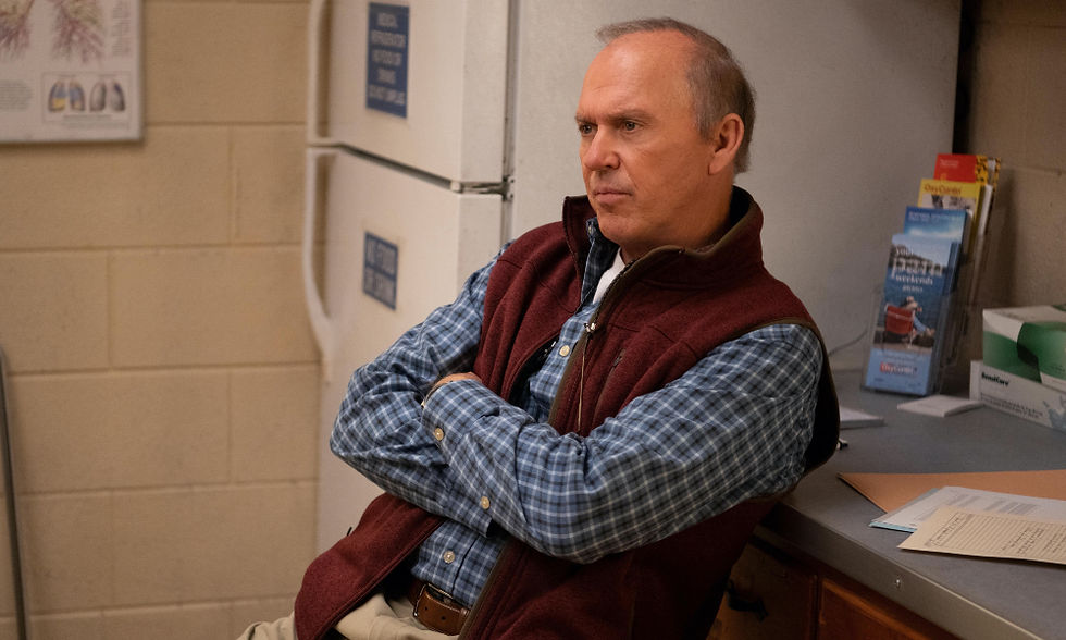 Michael Keaton sitting and leaning next to a fridge