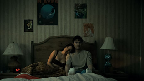 Inde Navarrette resting her on Michael Johnston's shoulder in bed, with posters on the wall above them.