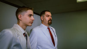 Jacob Tremblay and Nick Offerman, rocking white suits, hanging out in a meeting room.