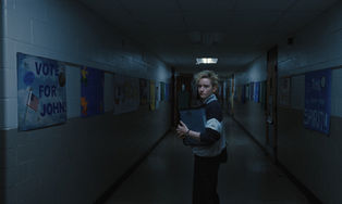 Julia Garner turning around and looking behind her in a dark school hallway.