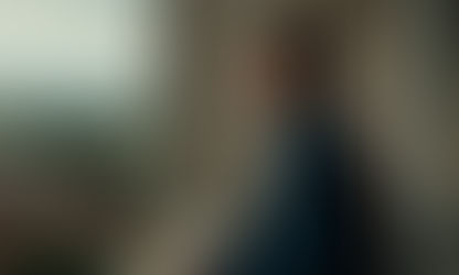 Robert Aramayo standing on a balcony several floors above the ground, looking at and taking in the view.