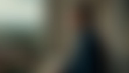 Robert Aramayo standing on a balcony several floors above the ground, looking at and taking in the view.