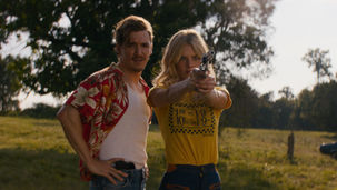 Samara Weaving points a gun on a meadow as Kyle Gallner watches behind her.