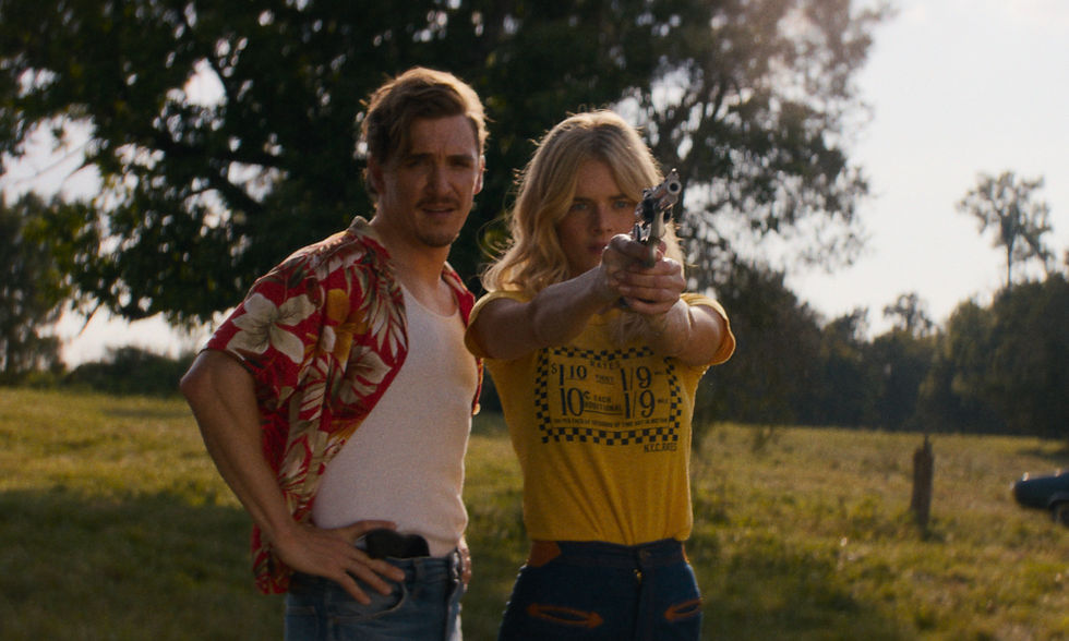 Samara Weaving points a gun on a meadow as Kyle Gallner watches behind her.