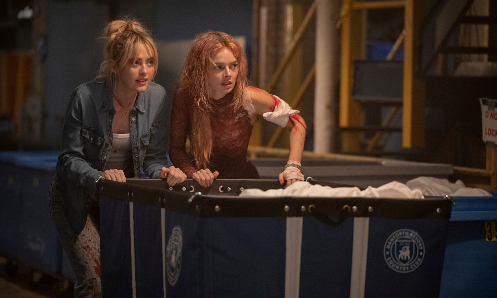 Disheveled Kathryn Newton and Samara Weaving pushing a laundry cart whilst covered in blood.