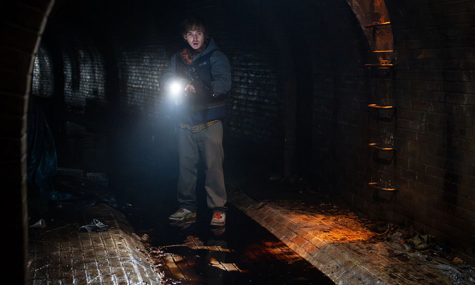 Austin Abrams hanging out in an underground sewer, holding a flashlight.