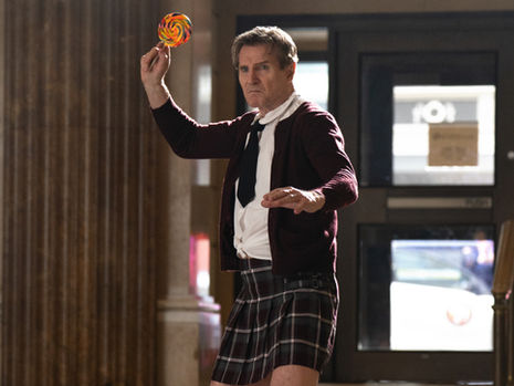 Liam Neeson wearing a children's school uniform, wielding a lollipop in his hand, ready to attack.