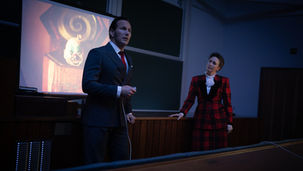 Patrick Wilson and Vera Farmiga standing in front of a projector screen in an auditorium.