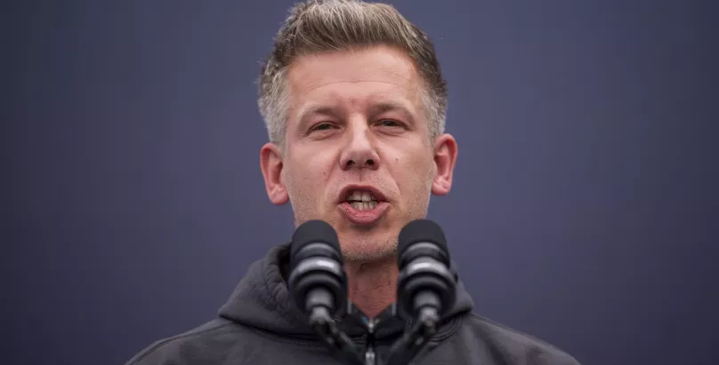 Hungarian voters lining up at a polling station ahead of the April 2026 parliamentary elections in Budapest, with campaign posters of Péter Magyar and Viktor Orbán visible.
