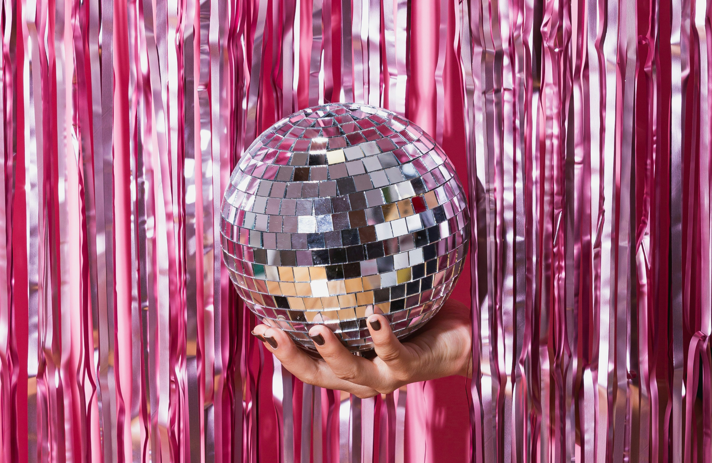 A hand peeking out from behind a curtain holding a disco ball