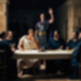 2. Brutus and the Conspirators Planning: In a dimly lit Roman villa with stone walls and a long table, Brutus sits at the head of the table in a white toga, his hand resting on his chin as he listens intently to Cassius, who is standing with his hand raised in persuasion.