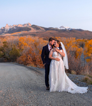a man lovingly holds a woman as they stand in front of a mountain range in colorado