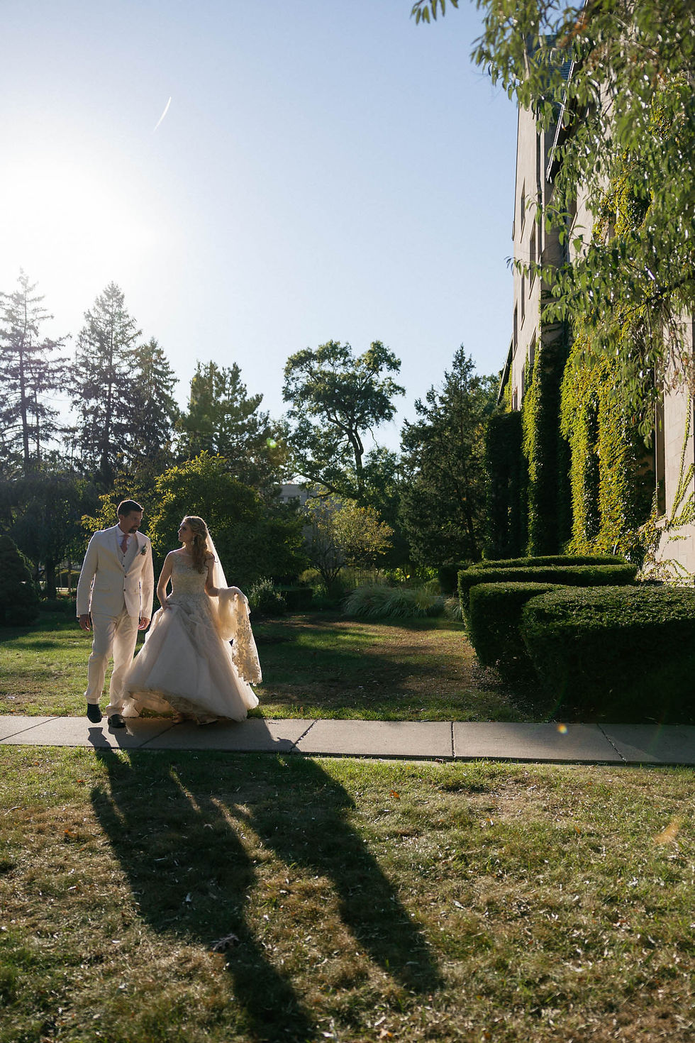 A bride and groom walk toward a European-looking building covered in ivy