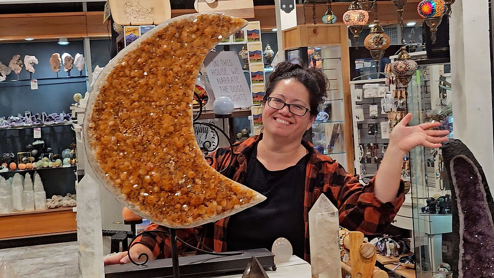 A person proudly displays a large, crescent-shaped gemstone in a shop filled with crystals and vibrant decor, radiating a sense of joy and warmth.