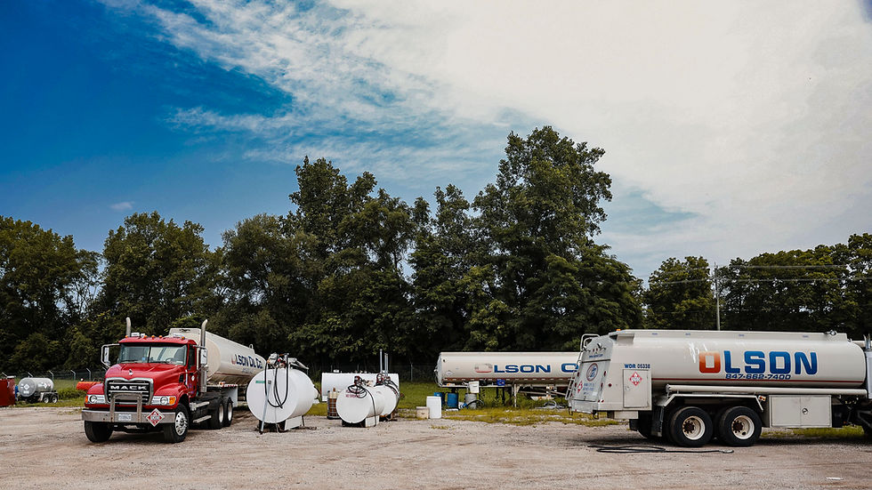 Red and white OLSON fuel tanker trucks parked under blue sky.
