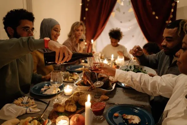 A group of friends from all different cultural backgrounds are sitting at the table enjoying their own holiday dinner. 