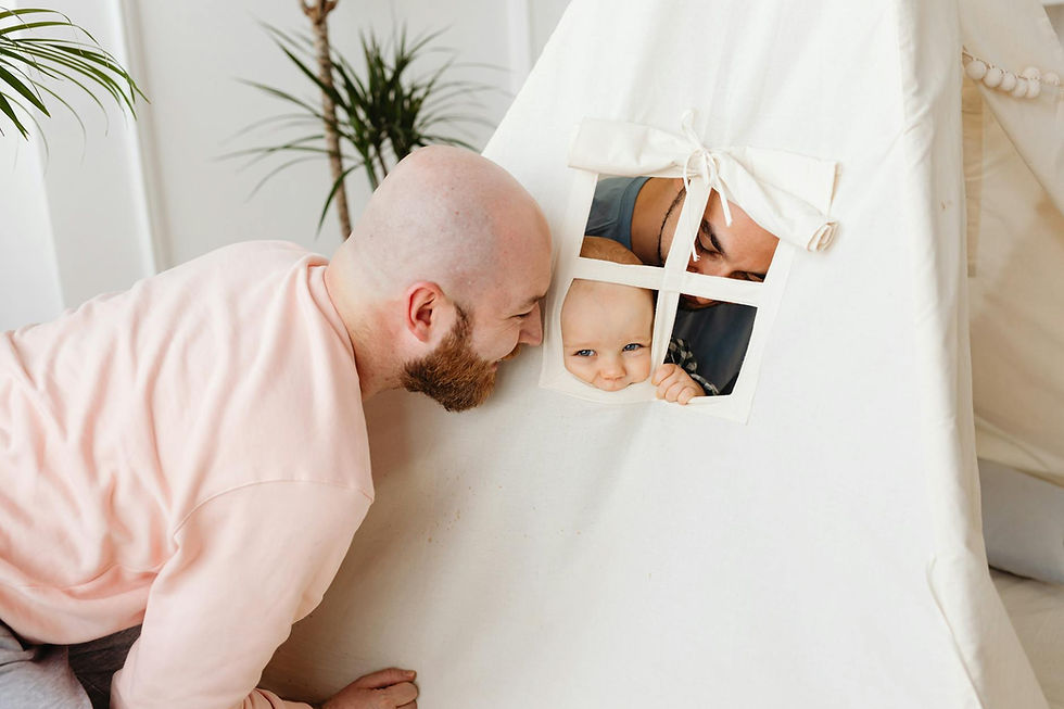A joyous couple, parents, smiling brightly as they play with their baby indoors, illuminated by soft natural light streaming through a window.