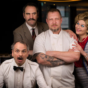 A man in a chef's jacket is surrounded by actors dressed as key characters from Fawlty towers