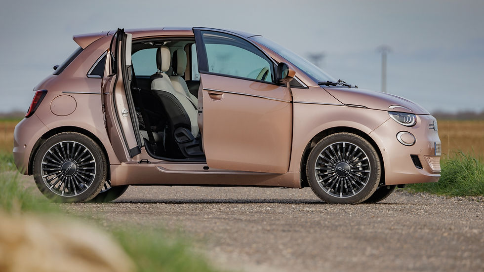 The image shows a metallic rose-colored Fiat 500e compact car with open doors and black rims parked outside on a paved area under a cloudy sky.
