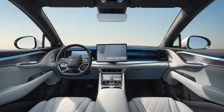 The image shows the interior of a modern BYD car with a steering wheel, two digital displays and blue ambient lighting. It is elegant and technologically advanced.