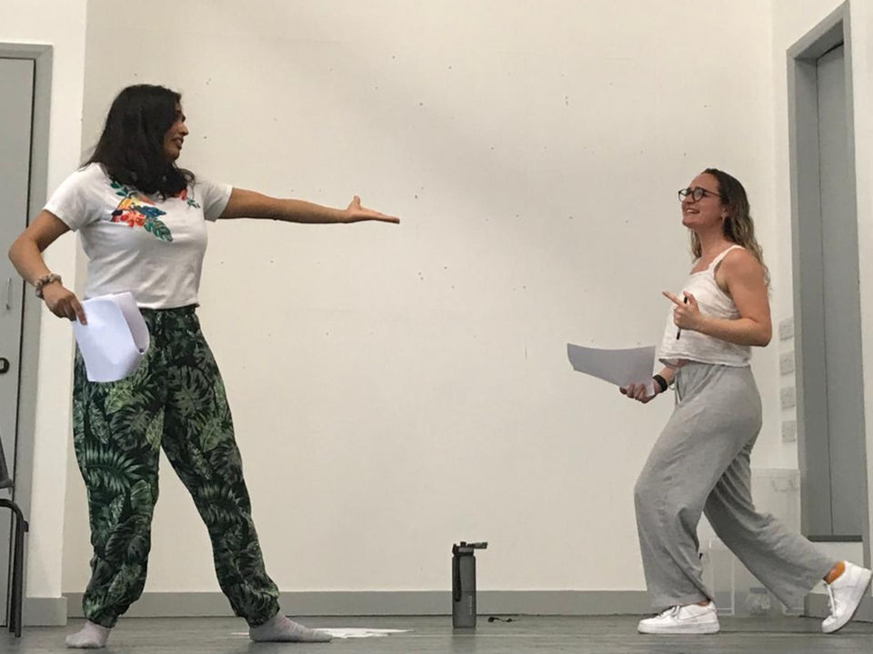 Two actors stand on a stage with scripts in hand, they are mid-movement.