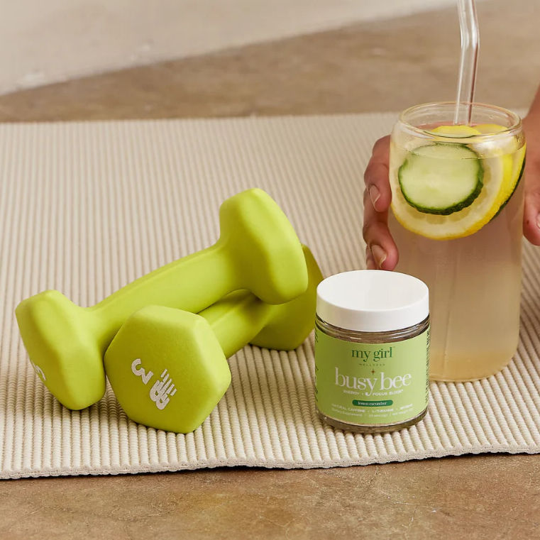 Lime green new balance wieghts next to busy be beverage and package, all sitting on yoga mat