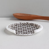 fused glass art spoon rest with black geometric pattern on a gray counter with a handmade wooden spoon