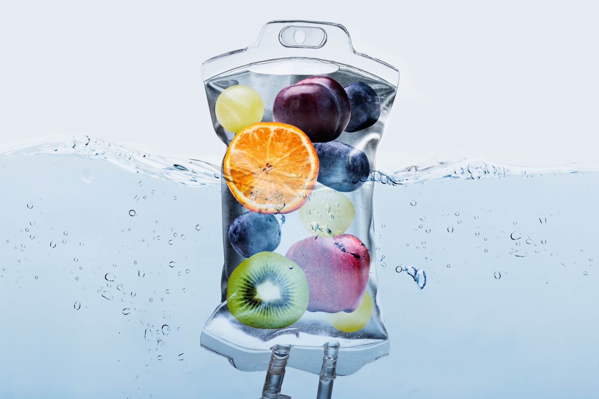 A conceptual IV bag filled with whole and sliced fruit suspended in clear water, illustrating vitamin infusion therapy