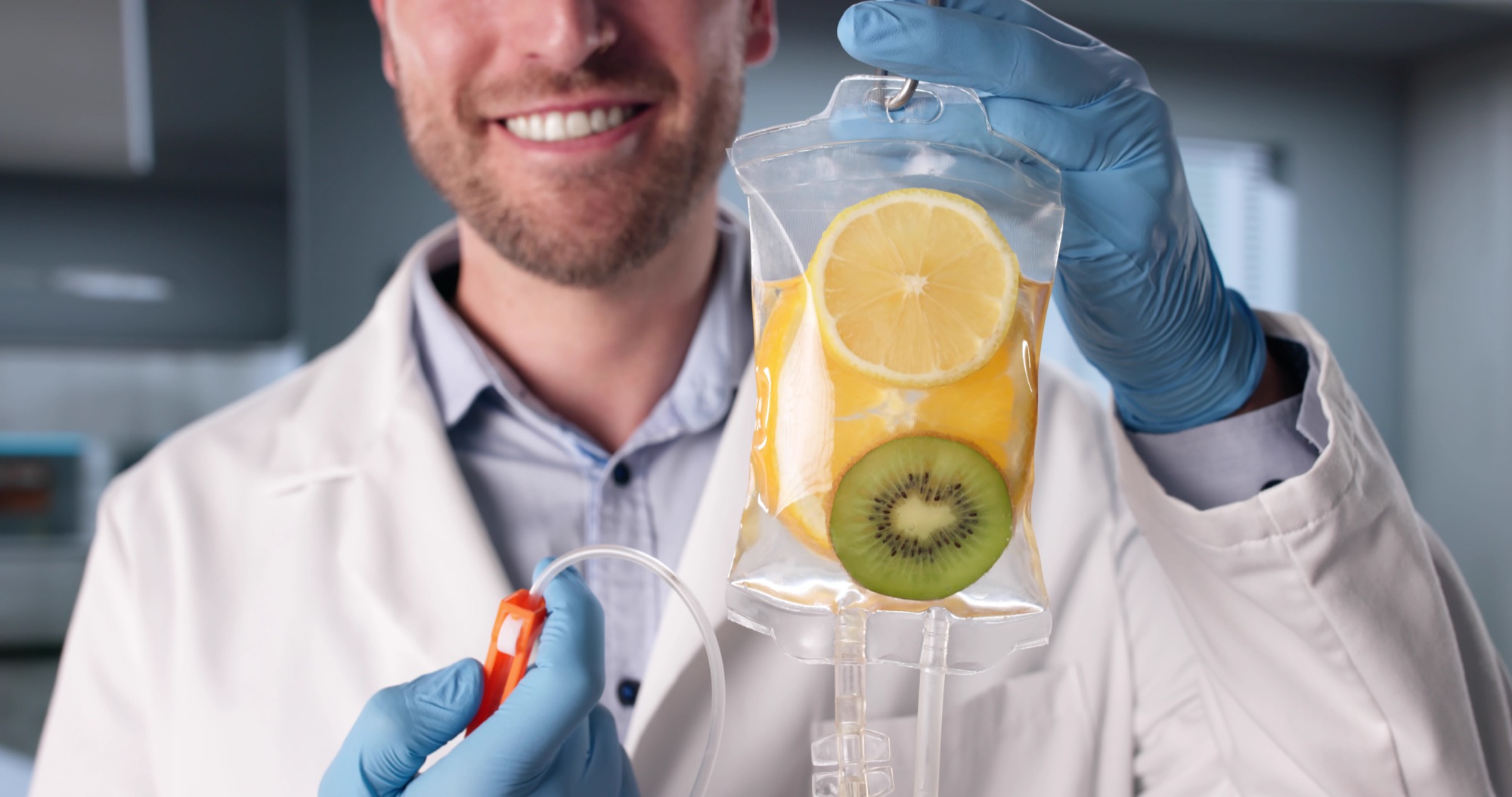 A smiling clinician holding an IV bag infused with lemon and kiwi slices