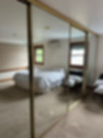 Clean mirrored closet doors reflecting a bedroom with a bed and windows.