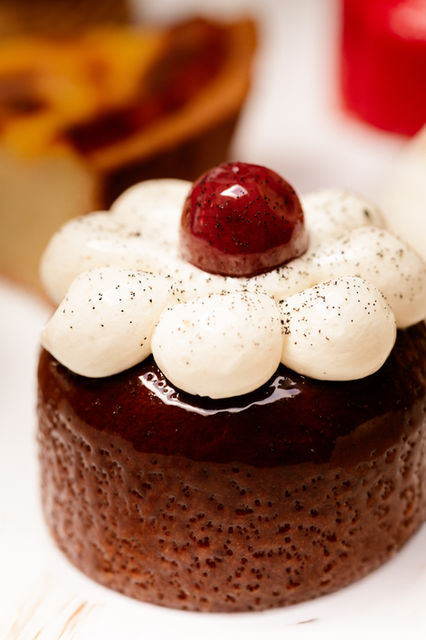 Petit gâteau au chocolat brillant avec crème blanche et cerise rouge.