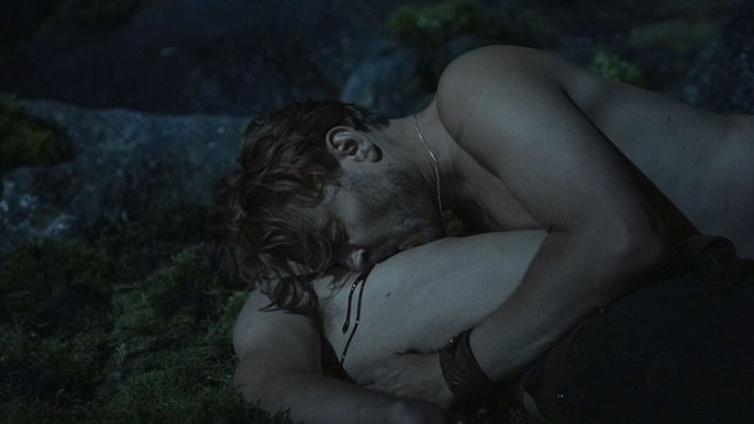 A white man with fair hair is biting on the chest of another white man and drawing blood.