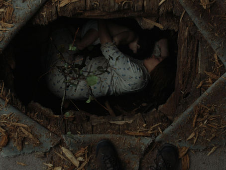 a white woman lies in the foetus position in a hole in the floor with her baby boy.