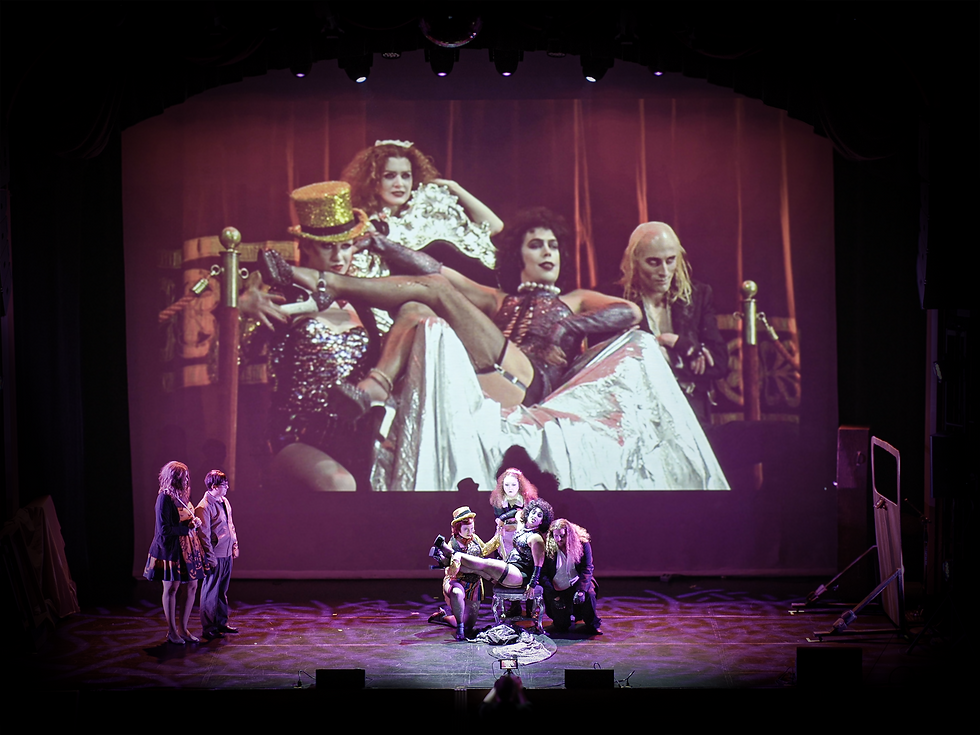 in front of a screen showing the rocky horror picture show is a live cast mirroring them.