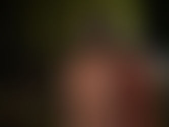 a possessed woman with grey skin, wispy hair and demonic eyes is in a pink dress standing near a wooded area.