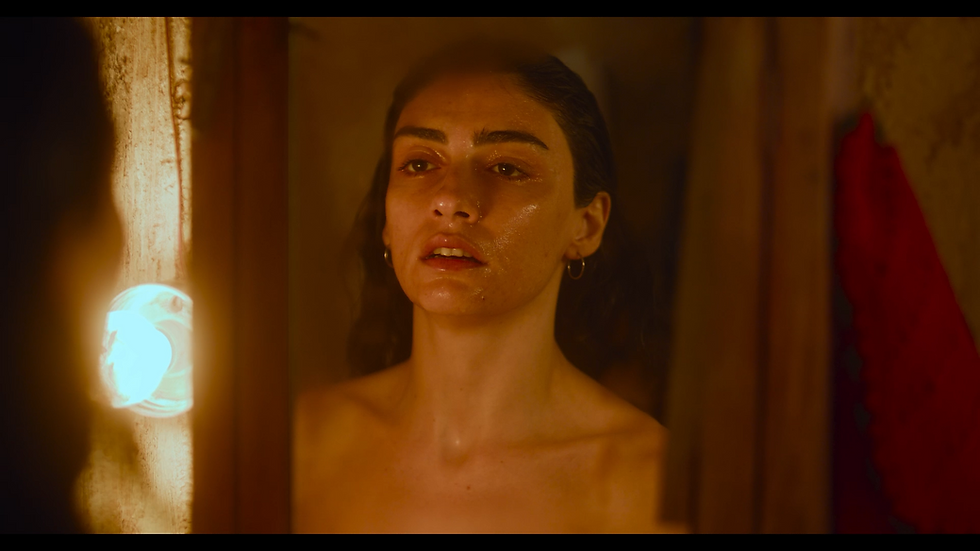 A Turkish woman with dark long hair is staring into a mirror bathed in warm light