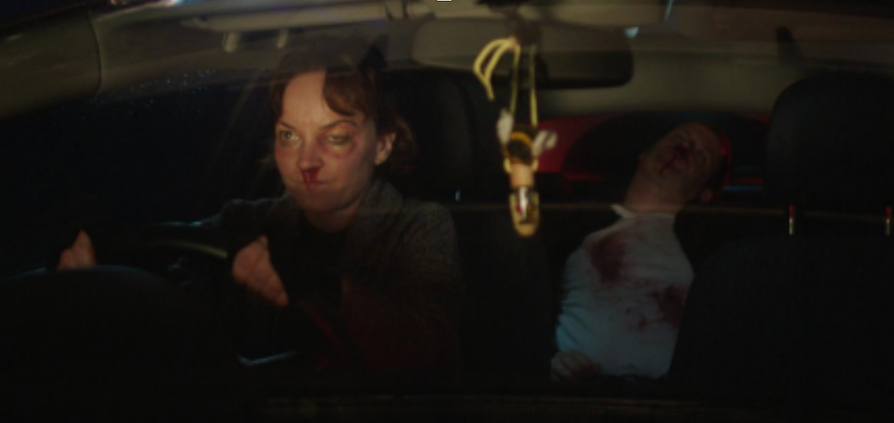 a woman with a bruised eye and a bloody nose is driving a car. in the back seat is a man passed out and bloody