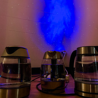 Three water kettles sitting on the ground in front of a blue galaxy light display