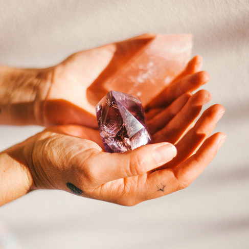 Hands holding a natural amethyst crystal point in soft natural light