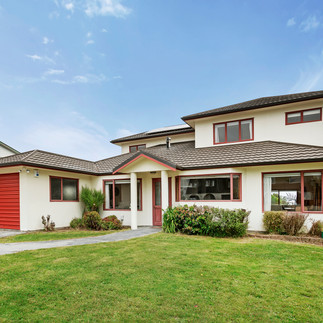 Sunny Four Bedroom Home Maungaraki – front exterior of 58 Cypress Drive with red trim, garage and flat lawn in a family-friendly street.