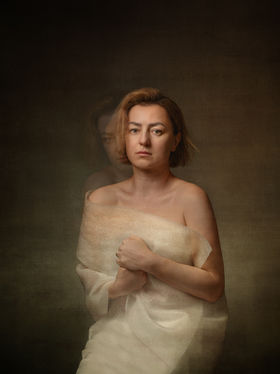 Self-portrait of a woman with a faint double exposure of her face slightly offset, creating a subtle duplicate behind the primary figure, suggesting internal doubling and quiet misalignment.