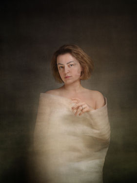 Self-portrait of a woman wrapped in translucent fabric with subtle duplication in the face and hand, suggesting shifting boundaries within a contained form.