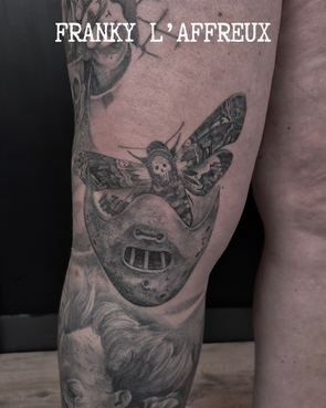 Tatouage du masque de Hannibal Lecter avec son papillon sur un genou, réalisé par Franky l'affreux, gérant des Pluies d'avril