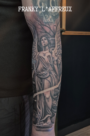 Tatouage style religieux d'une statue d'ange sur un avant-bras extérieur, réalisé par Franky l'affreux, gérant des Pluies d'avril