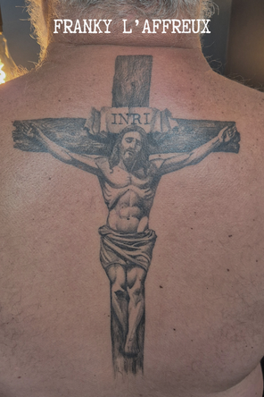 Tatouage style religieux d'un Christ en croix sur un haut de dos, réalisé par Franky l'affreux, gérant des Pluies d'avril