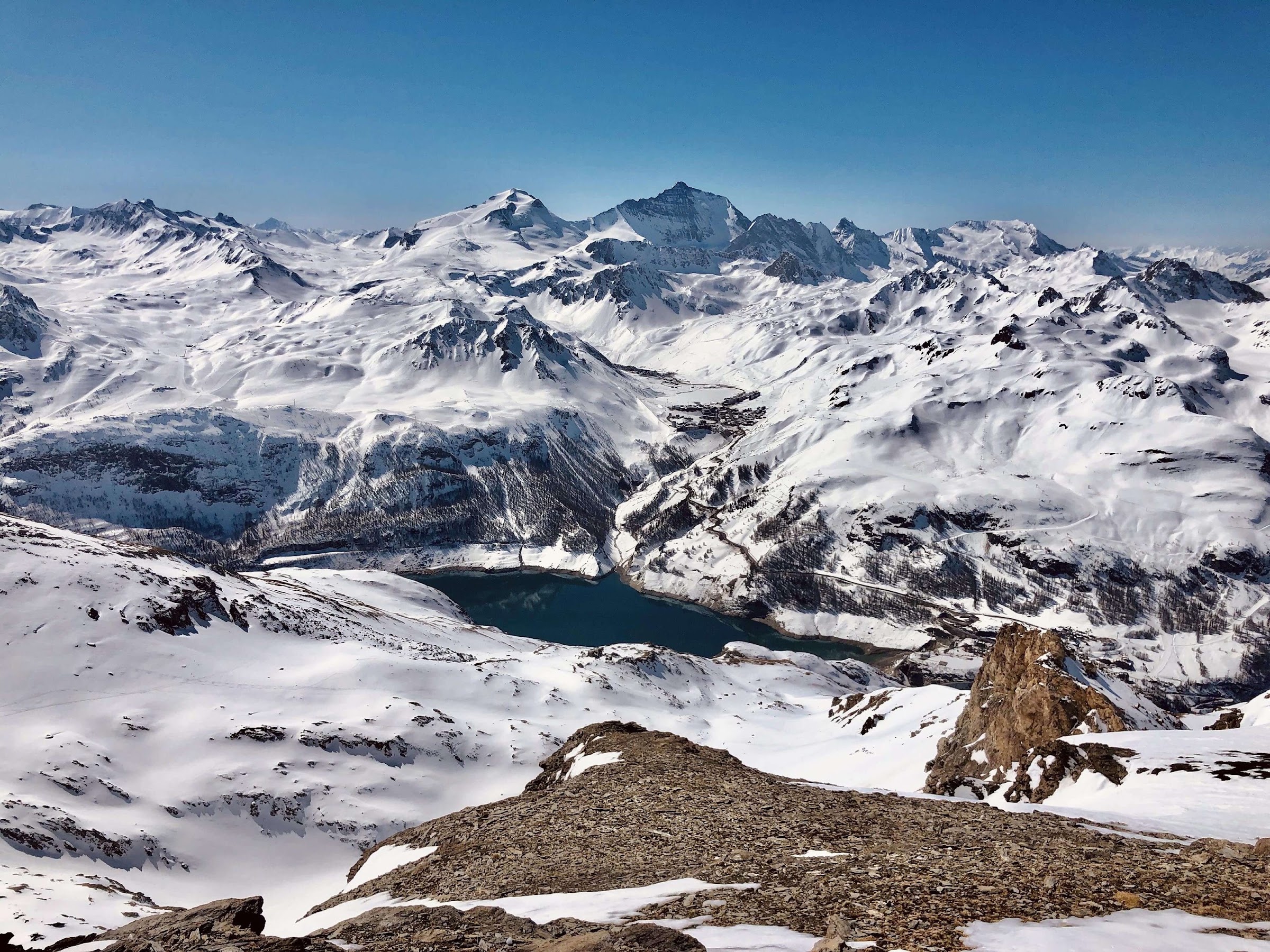 Der Stausee Lac du Chevril und verschneite Gipfel, von einem felsigen Grat in der Haute-Tarentaise aus gesehen